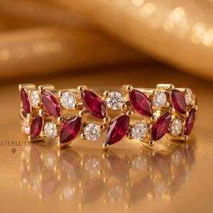 May include: A gold ring with alternating marquise-cut red gemstones and round white gemstones. The ring is set against a gold background, with the brand name "ATELIERLUXEIN" visible.