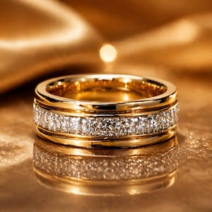 May include: A gold ring with a band of sparkling white gemstones. The ring is set against a golden background, reflecting the light. The ring's design features a double band with a row of gemstones in the middle.