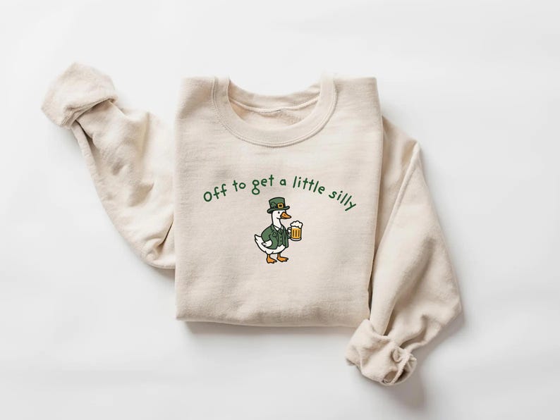 May include: Cream-colored sweatshirt with the phrase "Off to get a little silly" in green script. A cartoon goose wearing a green hat and jacket, holding a beer mug, is printed on the front.