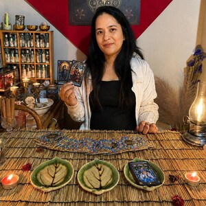 May include: A set of three green ceramic leaf-shaped dishes arranged on a bamboo mat. Two dishes are empty, while the third holds a tarot card. A deck of tarot cards is fanned out behind the dishes, and two lit tea light candles are placed nearby.