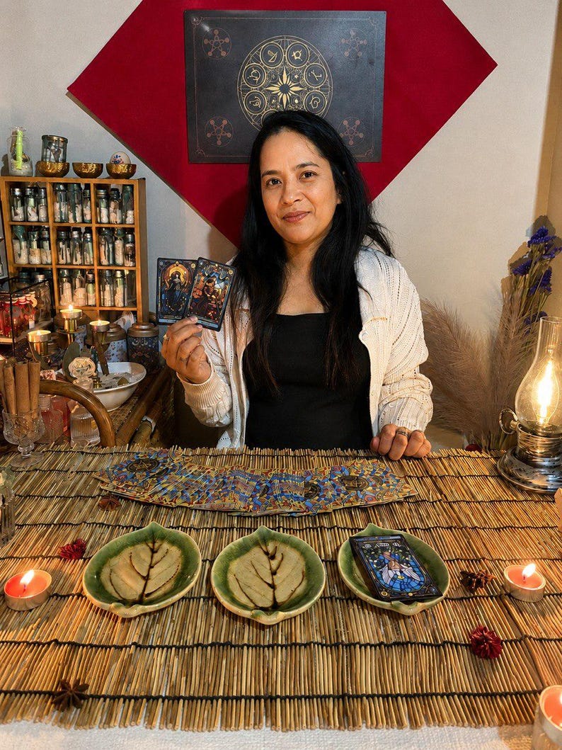 May include: A set of three green ceramic leaf-shaped dishes arranged on a bamboo mat. Two dishes are empty, while the third holds a tarot card. A deck of tarot cards is fanned out behind the dishes, and two lit tea light candles are placed nearby.