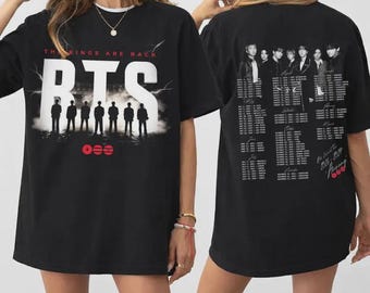 May include: Black t-shirt featuring the text "THE KINGS ARE BACK" and "BTS" in white block letters. The front design includes silhouettes of seven figures. The back of the shirt displays a group photo and a tour schedule.