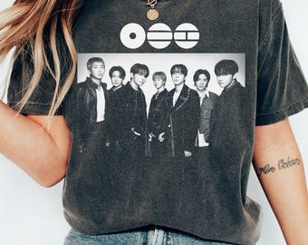 May include: Dark gray t-shirt featuring a black and white image of a group of people. Above the image are three white symbols. The shirt is a crew neck style.