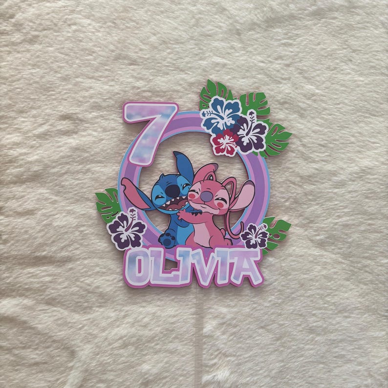 May include: A colorful cake topper featuring the characters Stitch and Angel, with the number 7 and the name Olivia. The design includes tropical flowers and leaves, with a purple and blue color scheme.