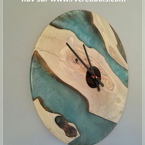 May include: Oval wooden wall clock with a teal resin river design. The clock features a natural wood grain pattern and black clock hands. The clock's face has a dark center with a red second hand.