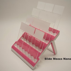 Puede incluir: Un portaobjetos Slide Mezza Nano rosa y blanco con divisores de plástico transparente. El soporte está diseñado para contener múltiples portaobjetos y tiene el texto "Slide Mezza Nano" impreso en la base.