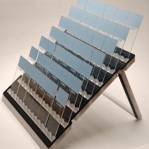 May include: Angled display stand with multiple clear, rectangular holders, each with a light blue insert. The stand is black and white with the text "SlideMate" visible on some holders. The stand is designed to hold multiple items.