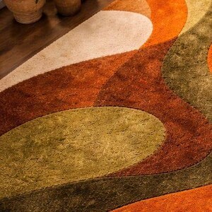 May include: A close-up of a retro-style rug with a geometric pattern. The rug features curved shapes in shades of orange, green, and cream. The rug is placed on a wooden floor, with several potted plants in the background.
