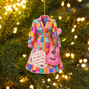 Könnte beinhalten: Ein flacher, hängender Schmuck in Form eines Kleides mit buntem Patchwork-Muster in Rosa-, Blau-, Gelb- und Orangetönen. Eine rosa Akustikgitarre ist vorne angebracht. Der Text lautet, I can see the light of a clear blue morning.