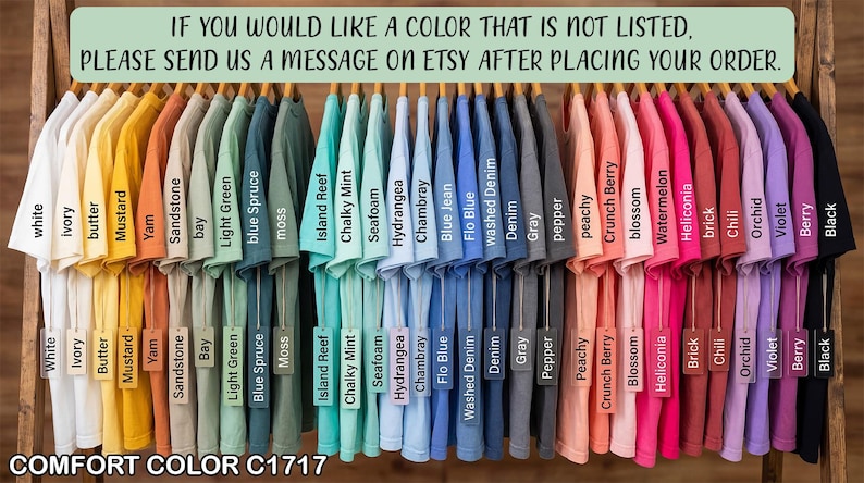 May include: A display of Comfort Color C1717 t-shirts in various colors, including white, mustard, blue spruce, and black, hanging on wooden hangers. The image includes text that reads, "If you would like a color that is not listed, please send us a message on Etsy after placing your order."