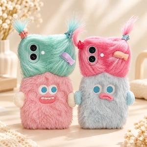 May include: Two fuzzy phone cases featuring plush textures and embroidered faces. The left case is mint green with a pink body, while the right case is bright pink with a light blue body. Both have tufts of hair with small star-shaped hair clips.