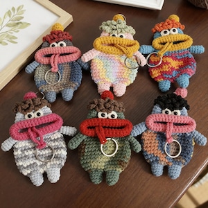 Puede incluir: Colección de seis llaveros de ganchillo hechos a mano con forma de criaturas caprichosas. Cada llavero presenta una combinación de colores única, incluyendo azul, rosa, amarillo y verde. Las criaturas tienen ojos grandes, bocas abiertas y un anillo para llaves.