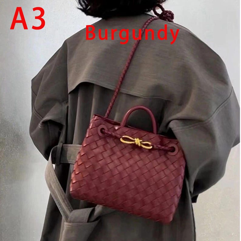 K&ouml;nnte beinhalten: Burgunderfarbene Handtasche mit gewebtem Design. Die Tasche hat einen oberen Griff und einen Schulterriemen. Ein goldfarbener Verschluss ziert die Vorderseite. Die Texte "A3" und "Burgundy" sind im Bild zu sehen.