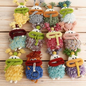 May include: A collection of handmade, colorful crochet keychains. Each keychain features a whimsical creature design with a round body, large mouth, and small antennae. The keychains are in various colors, including yellow, blue, green, and pink.