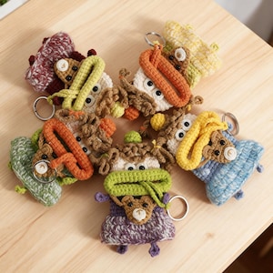 Puede incluir: Una colección de llaveros de ganchillo hechos a mano en varios colores, incluyendo naranja, verde, amarillo y morado. Cada llavero presenta un diseño de animal caprichoso con ojos grandes y un pequeño anillo de metal para sujetar llaves.