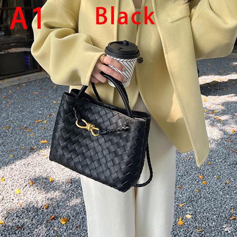K&ouml;nnte beinhalten: Schwarze Tote Bag aus geflochtenem Leder mit goldfarbenem Verschluss. Die Tasche hat einen geflochtenen Griff und einen abnehmbaren Schulterriemen. Die Tasche wird von einer Person gehalten, die eine gelbe Jacke tr&auml;gt. Das Wort "Black" ist rot geschrieben.