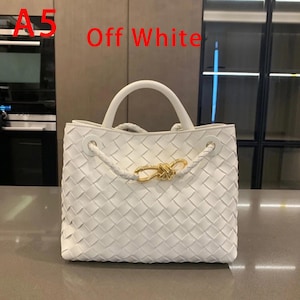 K&ouml;nnte beinhalten: Cremefarbene Handtasche mit gewebtem Design. Die Tasche hat einen oberen Griff, geflochtene Seildetails und einen goldfarbenen Verschluss. Der Text "Off White" ist sichtbar.