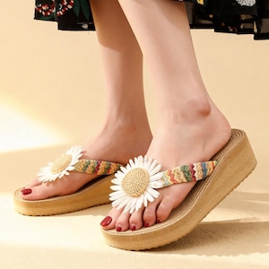May include: Wedge sandals with a woven platform and a large daisy accent. The straps feature a colorful woven design. The sandals have a beige platform and a white and yellow daisy flower on the top.