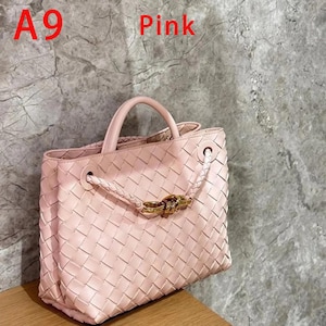 K&ouml;nnte beinhalten: Eine rosa gewebte Handtasche mit einem oberen Griff und einem geflochtenen Riemenverschluss. Die Tasche hat einen goldfarbenen Verschluss und das Wort "Pink" in roter Schrift. Die Tasche besteht aus einem gewebten Material.