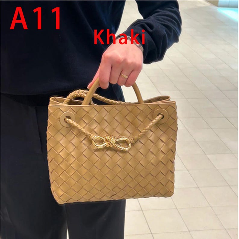 K&ouml;nnte beinhalten: Beigefarbene, gewebte Handtasche mit geflochtenem Henkel und dekorativem goldfarbenem Schleifenverschluss. Die Tasche hat eine quadratische Form und ein strukturiertes Design. Der Text "A11" und "Khaki" sind sichtbar.