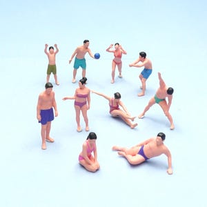 Pode incluir: Um conjunto de dez figuras de plástico em miniatura representando pessoas em trajes de banho envolvidas em várias atividades de praia. As figuras estão em poses diversas, incluindo em pé, sentadas e alongando, vestindo calções de banho e biquínis coloridos.