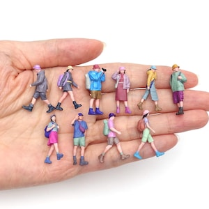 Könnte beinhalten: Eine Sammlung von zehn Miniatur-Kunststofffiguren, die Wanderer in verschiedenen farbenfrohen Outfits mit Hüten, Rucksäcken und Freizeitkleidung darstellen und in zwei Reihen angeordnet sind. Jede kleine Figur ist in einer Gehbewegung dargestellt.