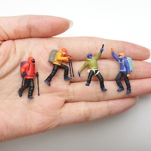 May include: Four miniature mountaineer figurines in colourful outdoor gear. One wears a red jacket with a purple backpack, one an orange jacket with a grey backpack, one a green jacket with an ice axe, and one a blue jacket with a light blue backpack.