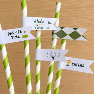 May include: A collection of paper straws with green and white stripes, adorned with small white flags. The flags feature golf-themed graphics and phrases like "Hole in One," "Par-Tee Time," and "Cheers," perfect for a golf-themed party.