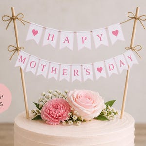 Op de afbeelding: Een caketopper met twee roze banners met de tekst "HAPPY MOTHER'S DAY". De banners zijn gespannen tussen houten stokjes en versierd met roze hartjes. De taart is versierd met roze bloemen.