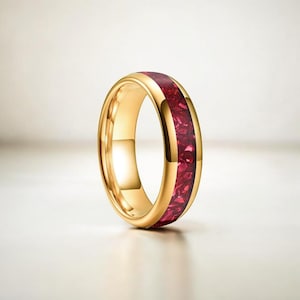 May include: A gold-colored ring with a vibrant red inlay. The ring has a polished, smooth surface and a band of red, textured material. The ring is displayed on a white background, highlighting its design.