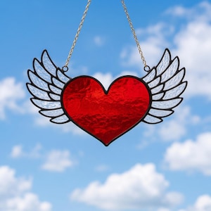 Puede incluir: Un corazón de cristal rojo con alas blancas y contorno negro, suspendido por una cadena dorada. Las alas son translúcidas. El fondo es un cielo azul claro con nubes blancas. Decoración de pared.
