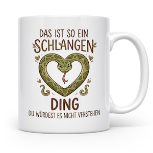 Könnte beinhalten: Eine weiße Keramiktasse mit einer grünen Schlange, die sich zu einem Herz geformt hat. Der Text lautet: DAS IST SO EIN SCHLANGEN DING DU WÜRDEST ES NICHT VERSTEHEN. Das Design enthält kleine dekorative Blätter und Herzen um die Schlange.