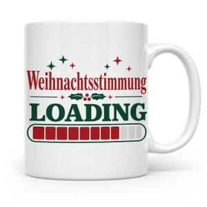 Könnte beinhalten: Ein weißer Keramikbecher mit dem roten Schriftzug "Weihnachtsstimmung" über dem grünen Wort "LOADING" sowie einer Ladebalkengrafik mit roten gefüllten und grauen leeren Segmenten, verziert mit kleinen roten und grünen Stern- und Stechpalmen-Symbolen.