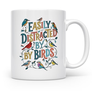 Könnte beinhalten: Ein weißer Keramikbecher mit einer farbenfrohen grafischen Illustration verschiedener Vögel, die auf dünnen, geschwungenen Zweigen sitzen. Der Text "EASILY DISTRACTED BY BIRDS" ist mittig in einer bunten, dekorativen Schriftart aufgedruckt.