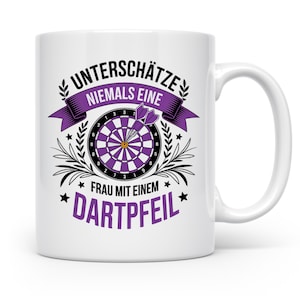 Könnte beinhalten: Weiße Keramik-Tasse mit Dartscheiben-Design und dem deutschen Text "UNTERSCHÄTZE NIEMALS EINE FRAU MIT EINEM DARTPFEIL" in Lila und Schwarz. Die Tasse hat einen gebogenen Henkel.