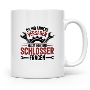 Könnte beinhalten: Weiße Keramik-Tasse mit schwarzer und roter Grafik. Die Grafik enthält Schraubenschlüssel, ein Zahnrad und den Text "DA WO ANDERE VERSAGEN - MÜSST IHR EINEN - SCHLOSSER - FRAGEN". Die Tasse hat einen gebogenen Griff.