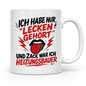 Könnte beinhalten: Eine weiße Keramiktasse mit schwarzem und rotem Text, der ICH HABE NUR LECKEN GEHÖRT UND ZACK WAR ICH HEIZUNGSBAUER lautet. Das Design zeigt eine Grafik von schwarzen Lippen mit herausgestreckter roter Zunge, akzentuiert durch rote Blitze.