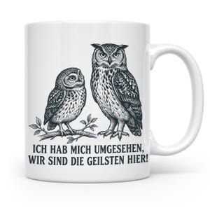 Könnte beinhalten: Weiße Keramiktasse mit einer schwarz-weißen Illustration von zwei Eulen auf einem Ast. Auf der Tasse steht der deutsche Text "ICH HAB MICH UMGEHESEN, WIR SIND DIE GEILSTEN HIER!"