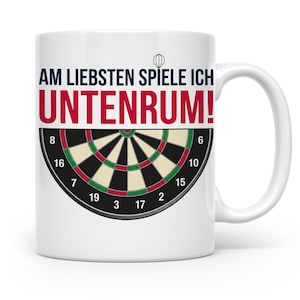 Könnte beinhalten: Weißer Keramikbecher mit Dartscheiben-Design und dem Text "AM LIEBSTEN SPIELE ICH UNTENRUM!" in Rot und Blau. Die Dartscheibe hat schwarze, grüne und rote Bereiche mit Zahlen.