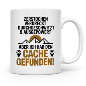 Könnte beinhalten: Weiße Keramik-Tasse mit einem schwarz-braunen Grafikdesign. Das Design beinhaltet Text, Berge und eine Sonne. Der Text lautet: "ZERSTOCHEN VERDRECKT DURCHGESCHWITZT & AUSGEPOWERT ABER ICH HAB DEN CACHE GEFUNDEN!"