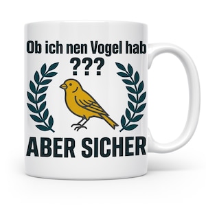 Könnte beinhalten: Ein weißer Keramikbecher mit einer gelben Vogelillustration, die zwischen zwei dunkelgrünen Lorbeerkränzen zentriert ist. Der Text über dem Vogel lautet "Ob ich nen Vogel hab ???" und der Text unter dem Vogel lautet "ABER SICHER" in fetten, dunkelgrünen Buchstaben.
