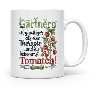 Könnte beinhalten: Ein weißer Keramikbecher mit einer Aquarellillustration einer Tomatenpflanze mit roten Tomaten und grünen Blättern. Der Text lautet Gärtnern ist günstiger als eine Therapie ...und du bekommst Tomaten! Unter dem Text befinden sich Illustrationen von einer Gartenschere, grünen Handschuhen und einer kleinen Schaufel.