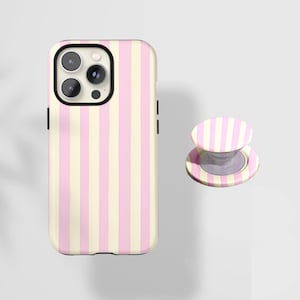 May include: A phone case and matching phone grip featuring a vertical striped pattern in alternating pastel pink and cream colors. The phone case has a black camera surround and black side buttons. The phone grip is round and has a clear base.