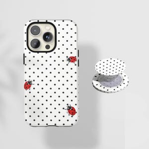 May include: White iPhone case with black polka dots and red ladybug illustrations. A matching white PopSocket with black polka dots is also shown. The phone case has a black camera border.