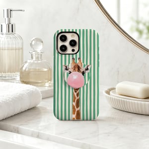 May include: A smartphone case featuring a vertical green and white striped pattern with a central graphic of a giraffe blowing a large pink bubblegum bubble. The case includes a circular phone grip attached over the giraffe's mouth area.