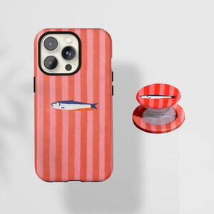 Könnte beinhalten: Ein Handyhüllen- und Pop-Socket-Set mit Sardinen-Motiv. Die Handyhülle hat ein rot-rosa gestreiftes Muster mit einer Sardinen-Illustration. Der Pop-Socket hat ein passendes Design. Die Handyhülle ist für ein Smartphone.