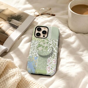 May include: A rectangular smartphone case featuring a patchwork design of various botanical patterns in shades of sage green, white, and soft blue. The case includes a circular collapsible grip attached to the centre and a camera cutout.