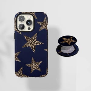 May include: A navy blue phone case and matching phone grip featuring a repeating pattern of leopard print stars. The phone case has a black border and cutouts for the camera. The phone grip is round with a pop-up feature.