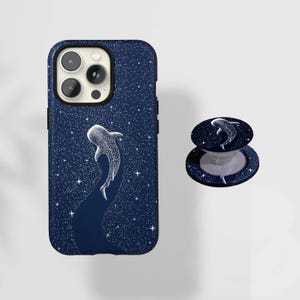 Peut inclure: Une coque de smartphone bleu foncé et un support de téléphone circulaire rétractable assorti. Les deux articles présentent une illustration de requin-baleine blanc entourée d'un champ dense d'étoiles blanches sur fond bleu marine.