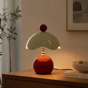 May include: A retro-style table lamp with a red spherical base and a light green, scalloped shade. A small red sphere tops the shade. The lamp has a gold-colored stem and is placed on a wooden surface.